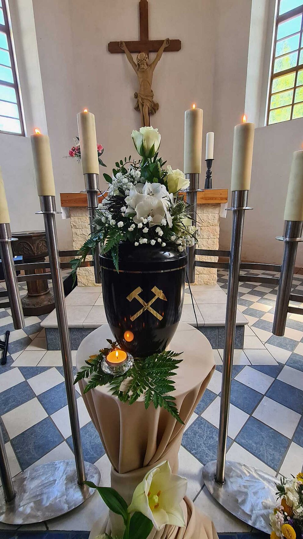 Mit Blumen dekorierte Urne von Kerzen umgeben, in der Kirche aufgebahrt.