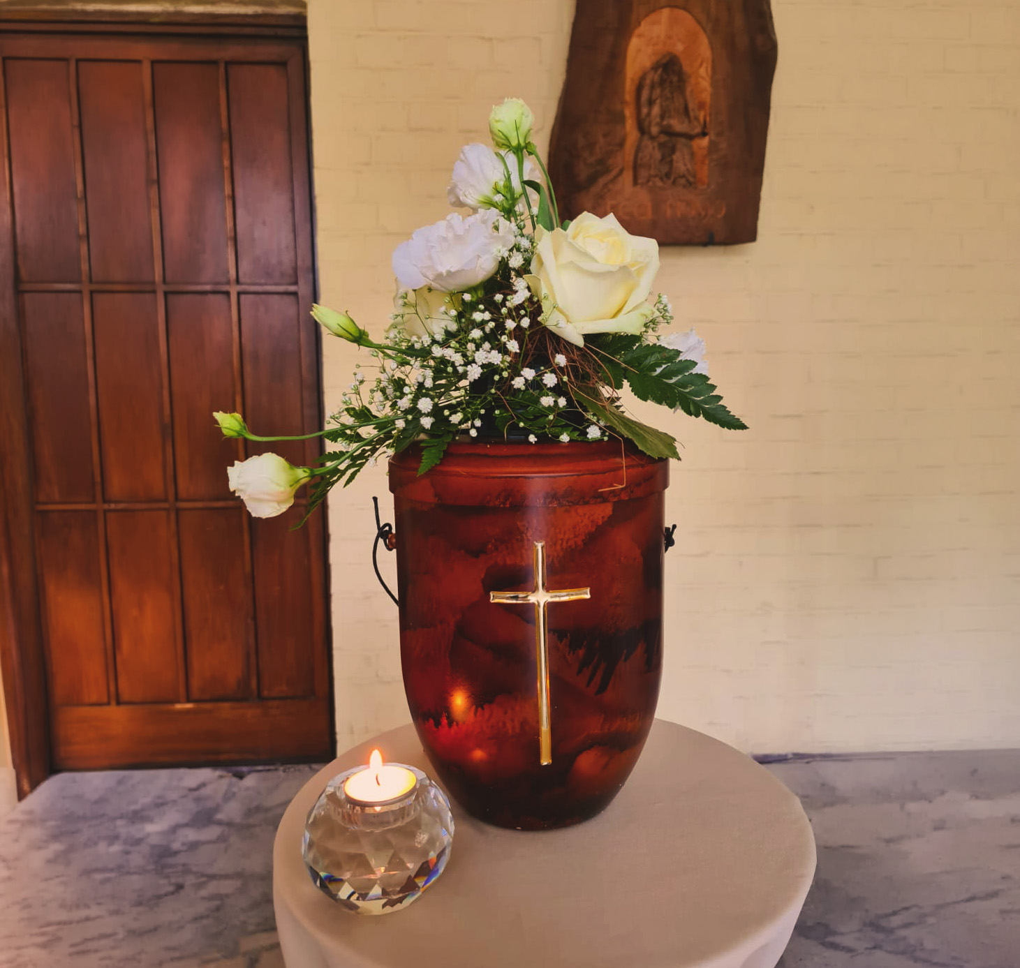 Urne mit Kruzifix und Blumendeko.