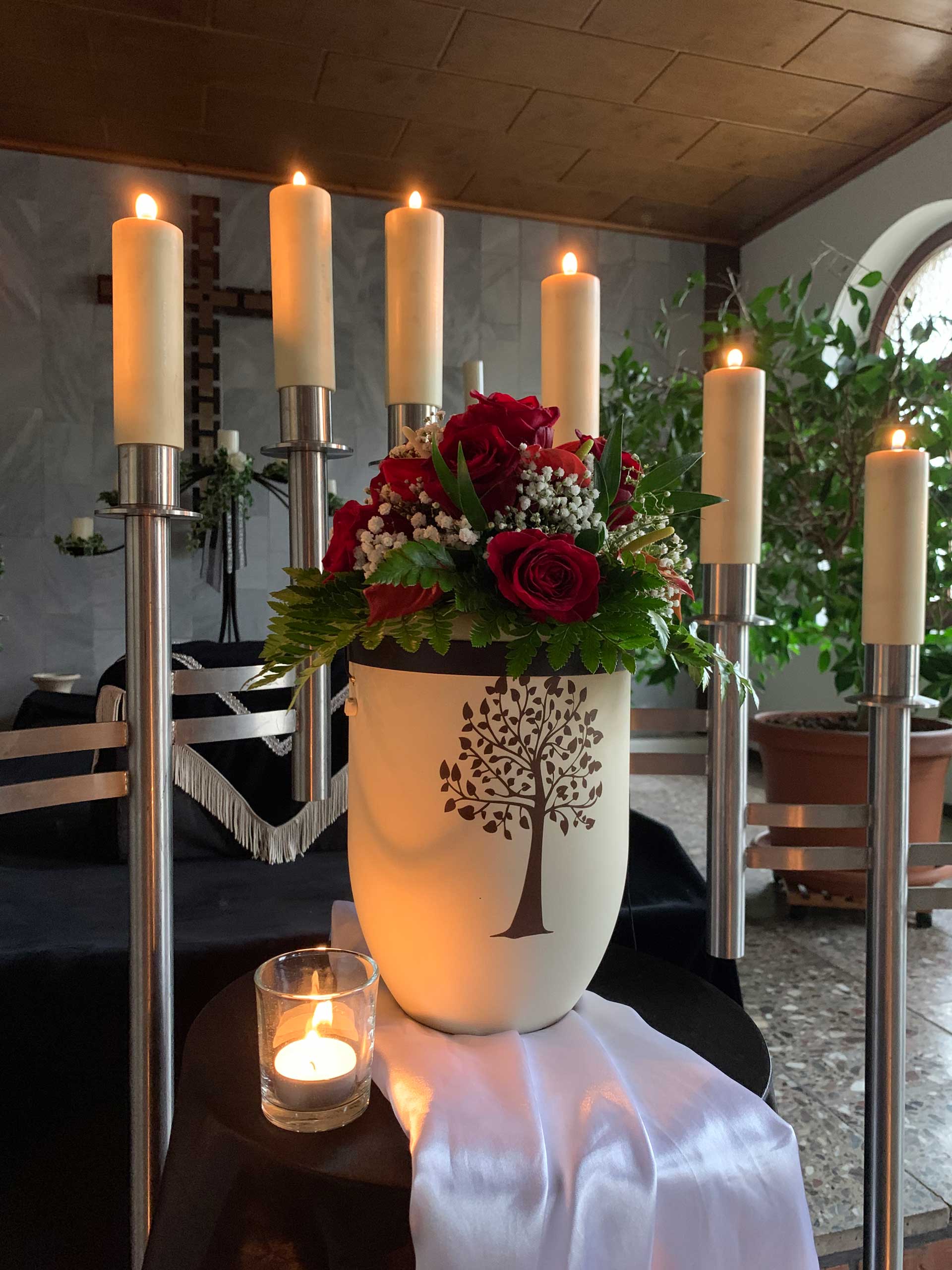 Urne mit Blumendeko stimmungsvoll aufgebahrt mit Kerzen.