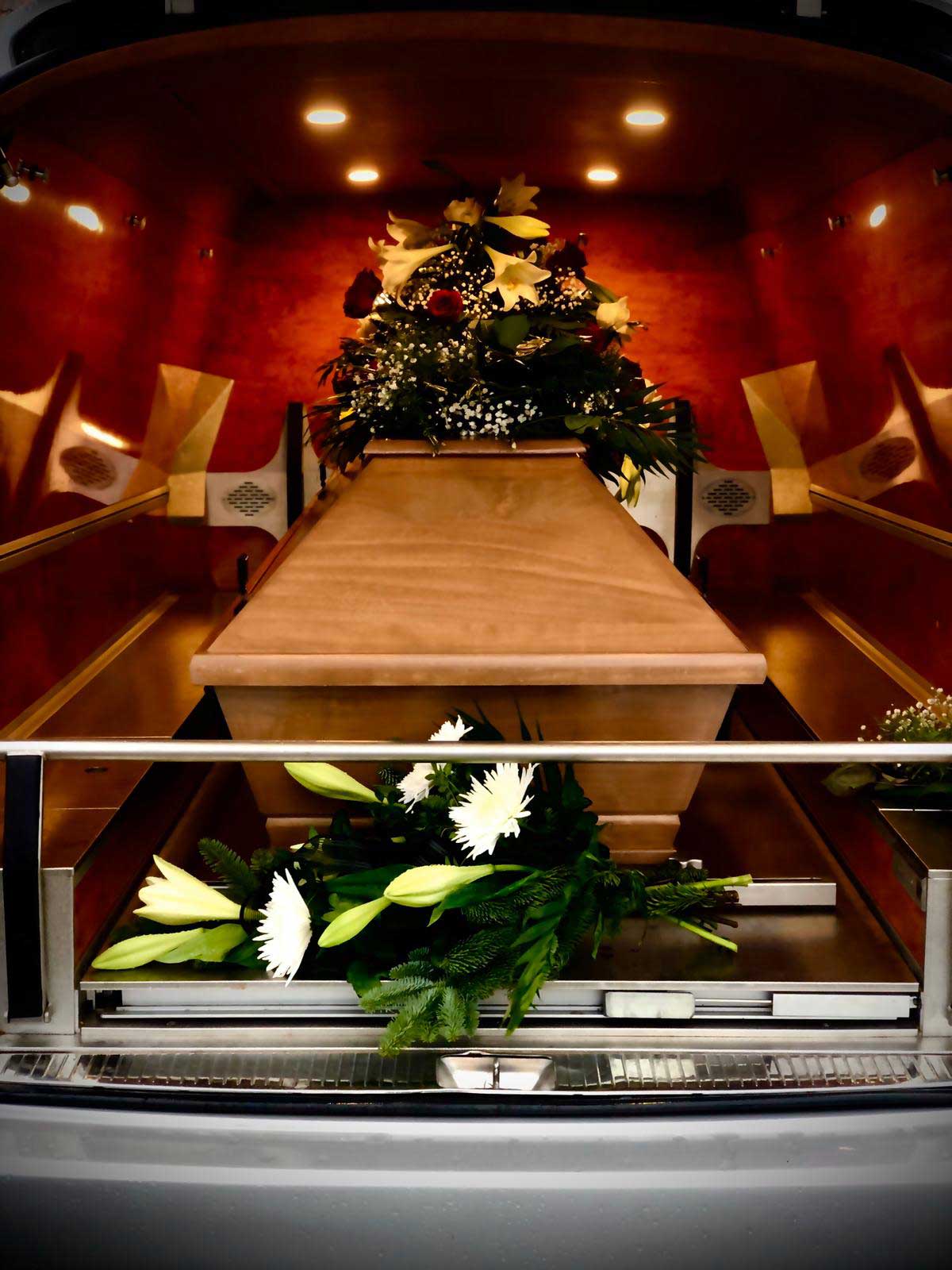 Sarg mit Blumendekoration in stimmungsvollem Licht in Transporthalterung des Bestattungsfahrzeugs.